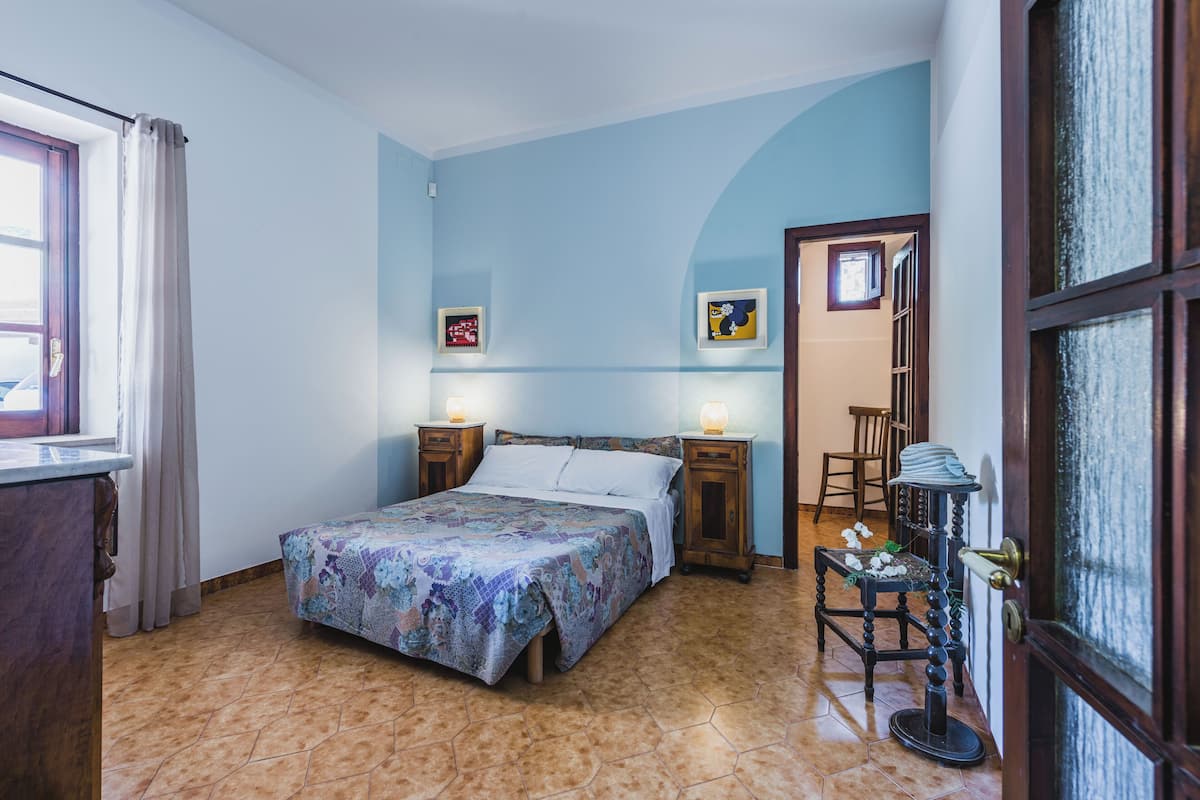 Ein Schlafzimmer mit einem Bett, zwei Nachttischen, einem Schminktisch, einem Sessel und einer Tür mit Fenster.