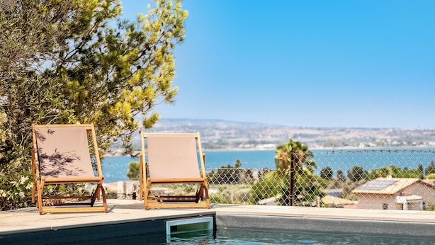 A poolside area with two wooden lounge chairs and a clear view of the ocean. - Galatea e Giardino delle Esperidi apartments with pool by Wonderful Italy (Syracuse)