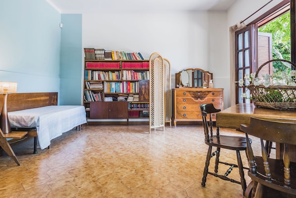 Una habitación acogedora con una cama, un aparador de madera, una estantería y una ventana con vistas a la vegetación.