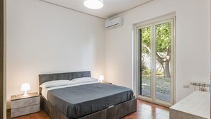 Een slaapkamer met een bed, nachtkastjes, een lamp, een airconditioner, een schuifdeur en een badkamergedeelte.