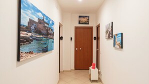 Un couloir orné d’un grand tableau représentant un paysage côtier, une porte en bois et une petite table sur laquelle repose un livre rouge.