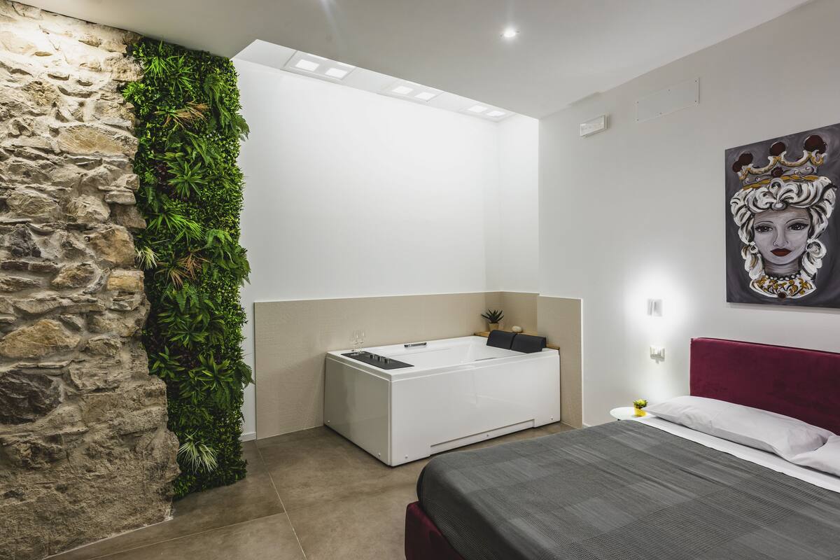 Ein modernes Schlafzimmer mit Steinwand, einem vertikalen Grünpflanzenwand, einer weißen Badewanne, einem roten Kopfteil und einem Bild an der Wand.