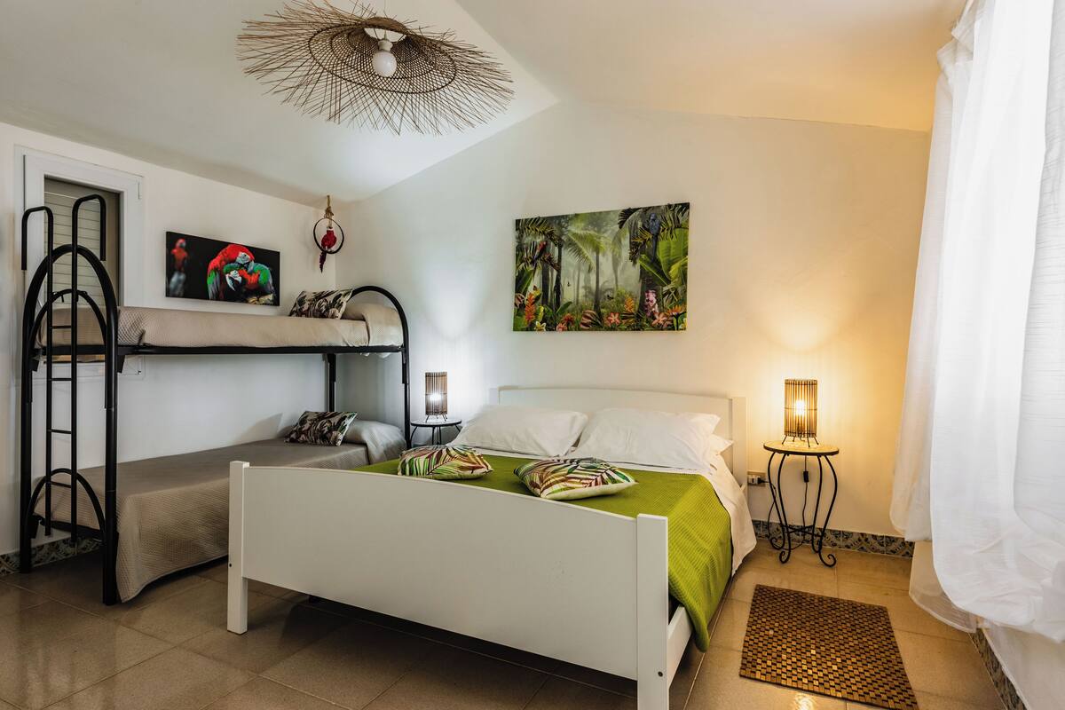A bedroom with a bunk bed, a single bed, a painting, and two bedside lamps.