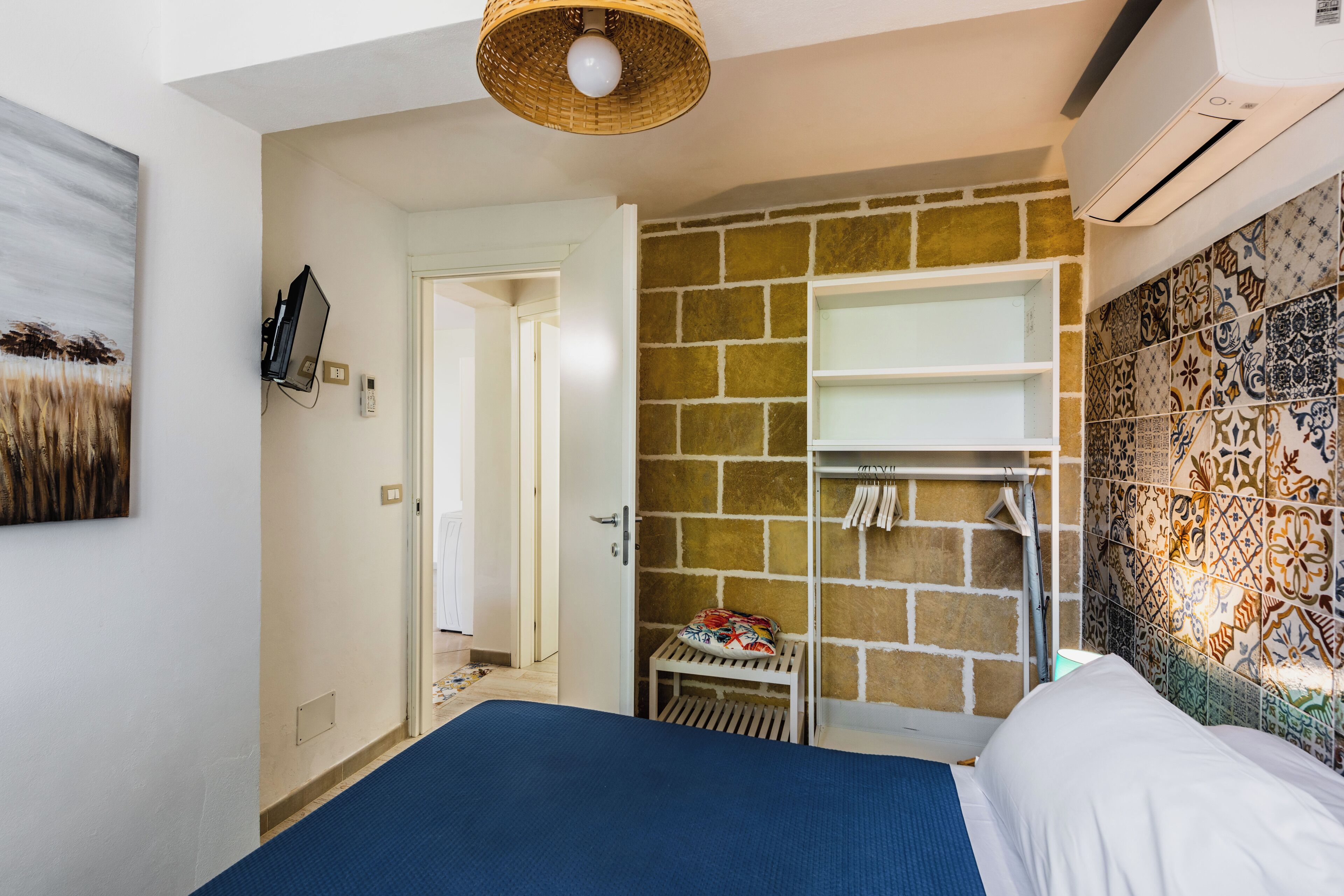 A bedroom with a bed, a wardrobe, a small table, and a wall-mounted shelf.