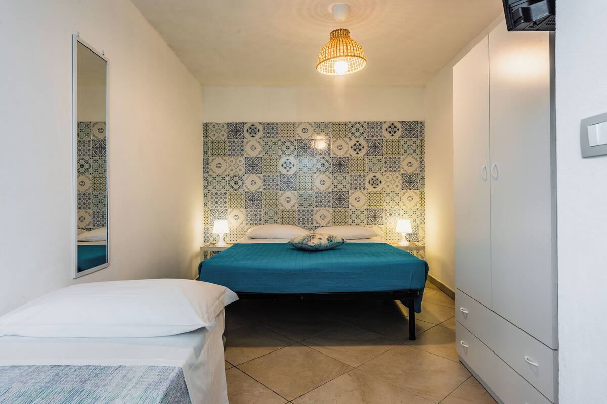 A bedroom with a bed, a wardrobe, a mirror, and patterned wall tiles.
