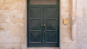 A double door with a brass handle, set in a stone wall with a small mailbox to the right.