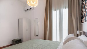 A hotel room with a bed, a bedside table, a mirror, an air conditioning unit, and a window with curtains.