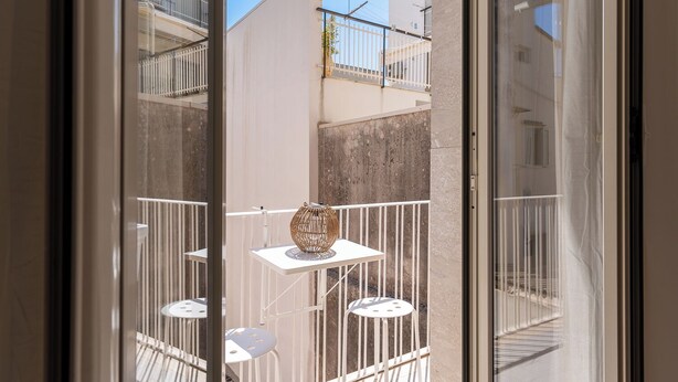 A balcony with a white table and chairs, a decorative vase, and a view of neighboring buildings.