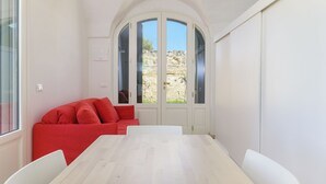 Ein Zimmer mit weißem Tisch, weißen Stühlen, einem roten Sofa und einem großen Bogenfenster mit Blick auf felsiges Gelände.
