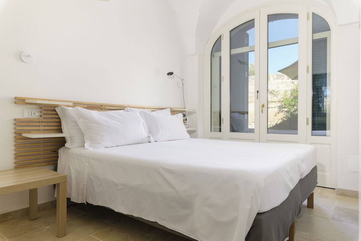 Un dormitorio con cama, mesita de noche y ventana con vistas al exterior.
