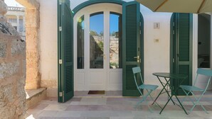 Ein Villa-Eingang mit einer weißen Tür, grünen Fensterläden und einem kleinen Tisch mit zwei Stühlen.