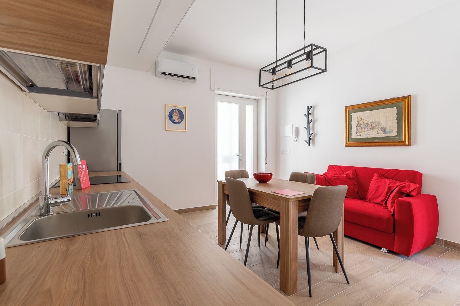 A modern kitchen with a dining area, a red sofa, and a pendant light.