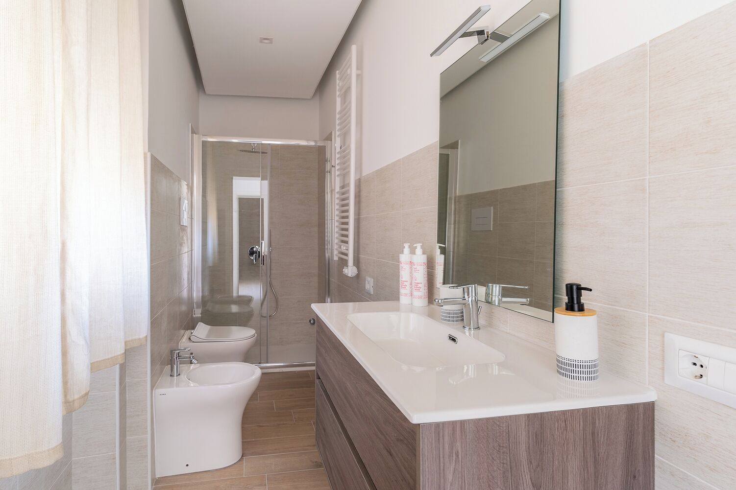 A modern bathroom with a glass shower enclosure, a toilet, and a vanity with a mirror and two sinks.