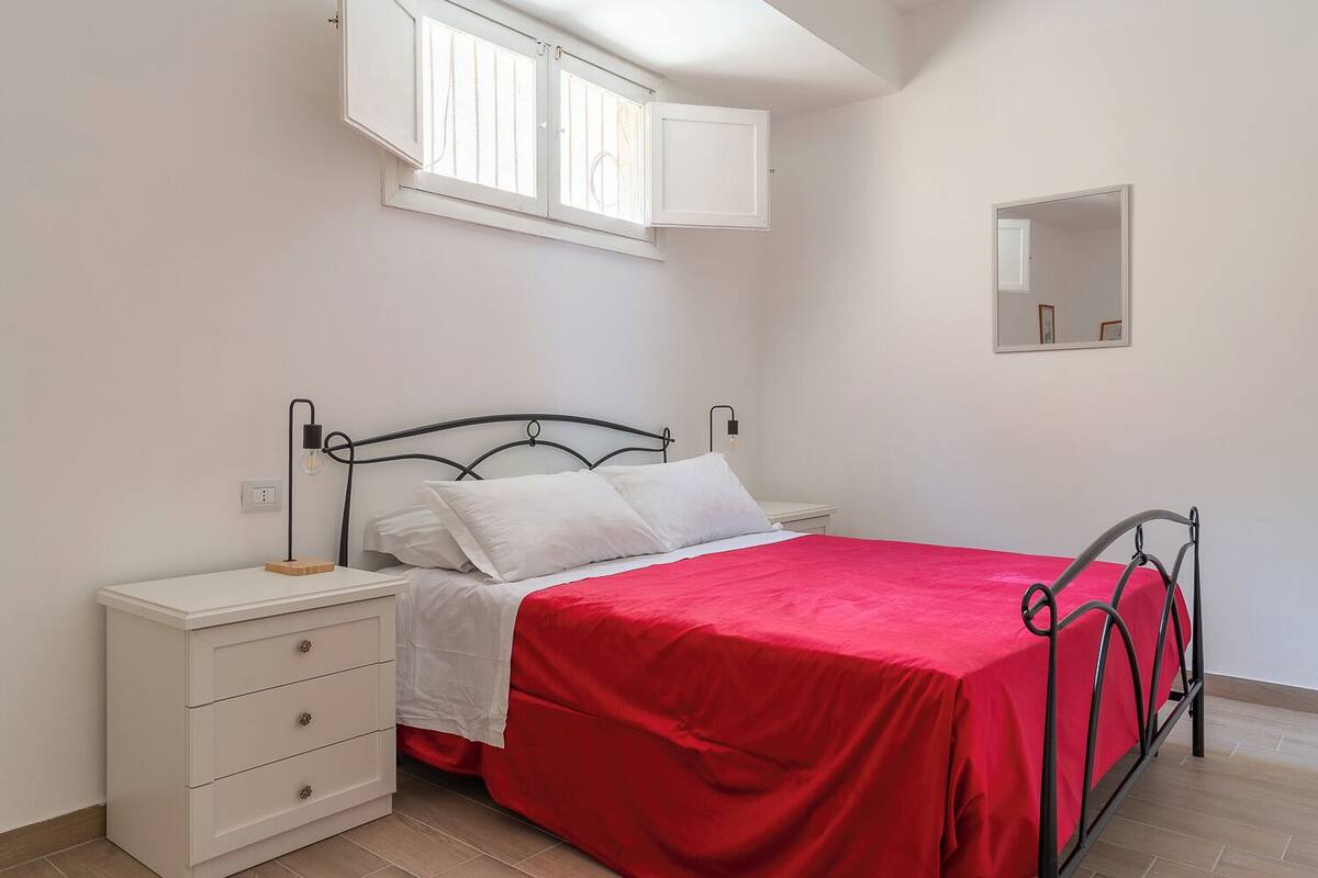 Un dormitorio con cama, mesita de noche, cómoda, ventana y espejo.