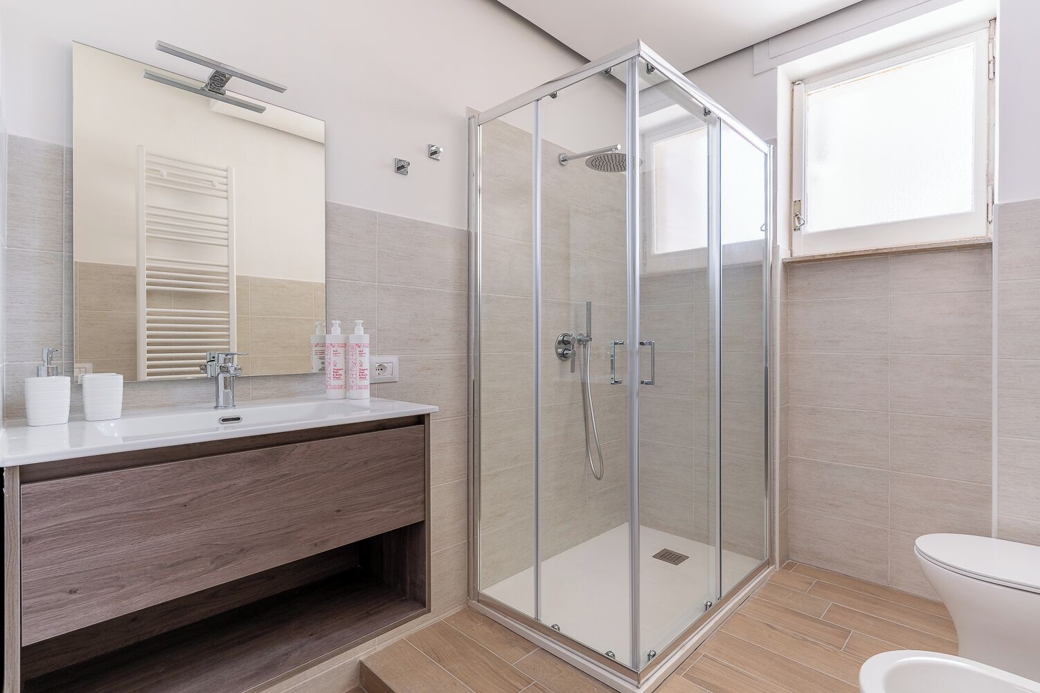 Une salle de bain moderne avec une douche à parois de verre, un meuble-lavabo en bois, un lavabo blanc et un grand miroir.