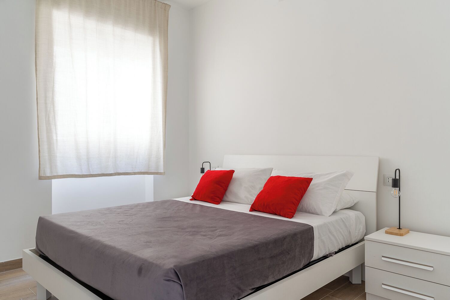 Een moderne slaapkamer met een bed, witte nachtkastjes en een nachttafeltje met een lamp.