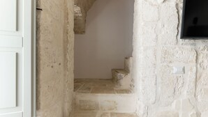 A narrow stone staircase leading to a higher level, with a white door on the left and a wall-mounted switch on the right. - Casetta Wilma by Wonderful Italy (Cisternino)
