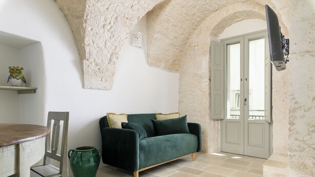 A room with a green sofa, a wooden chair, a green vase, and a white door with a balcony view. - Casetta Wilma by Wonderful Italy (Cisternino)