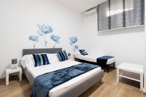 A bedroom with a large bed, two bedside tables, a small table, and a wall-mounted air conditioning unit.