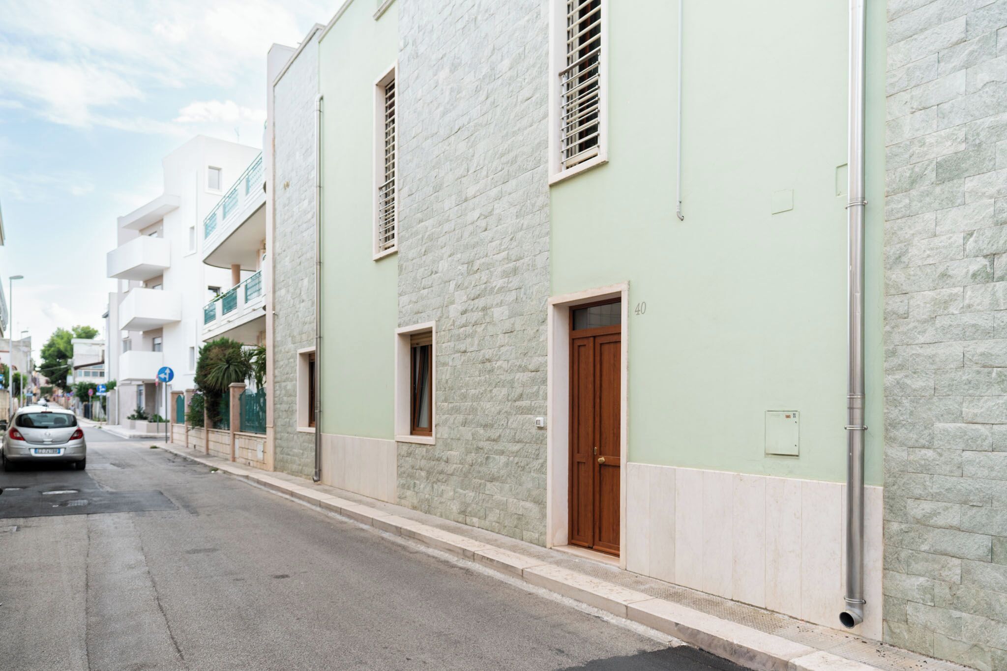 Une rue bordée d’un immeuble dont la façade est en pierre, avec une porte en bois et un balcon.