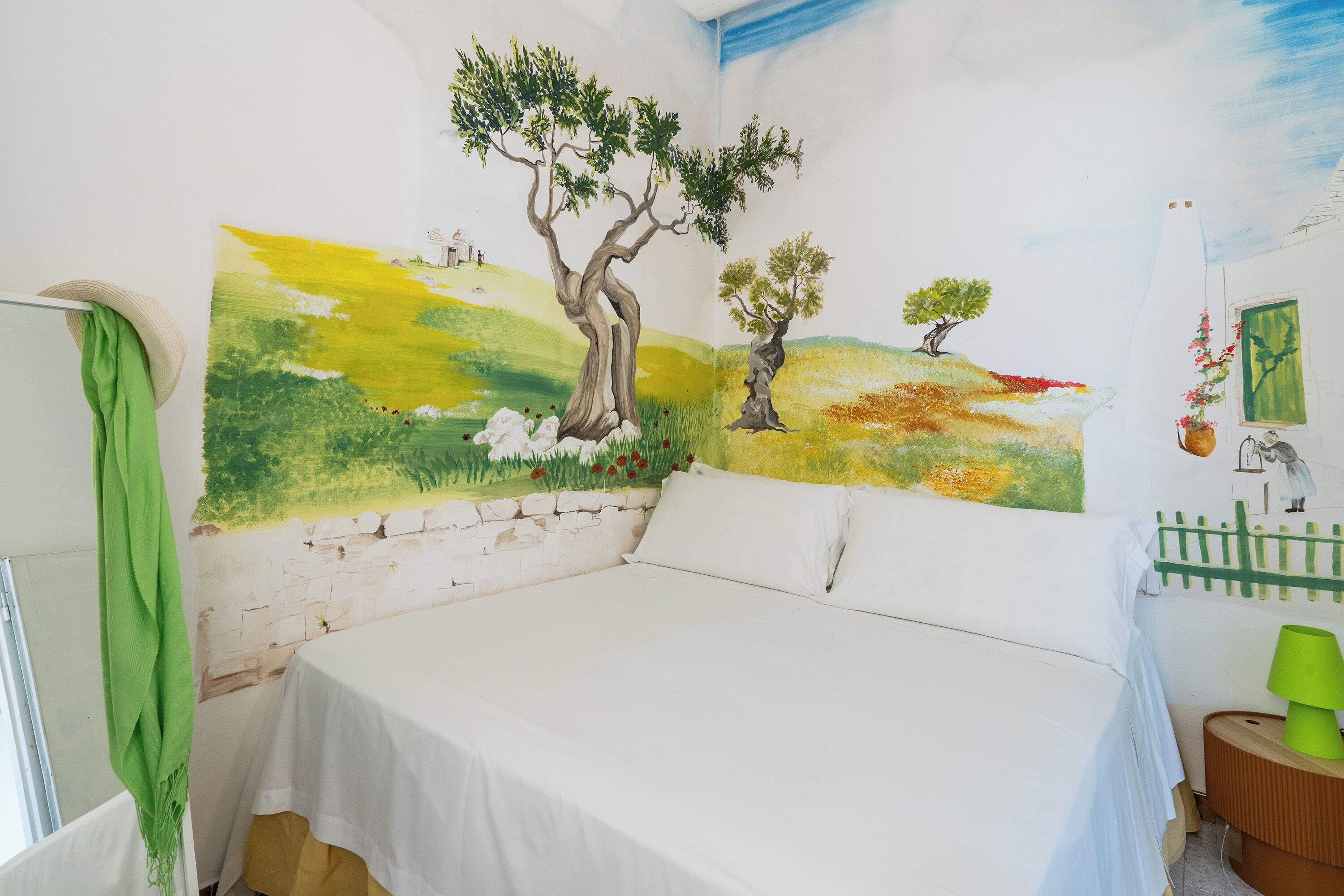 A bedroom with a large bed, a green wall hanging, and a mural of trees and a landscape.