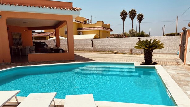 A swimming pool with white lounge chairs and a covered seating area.