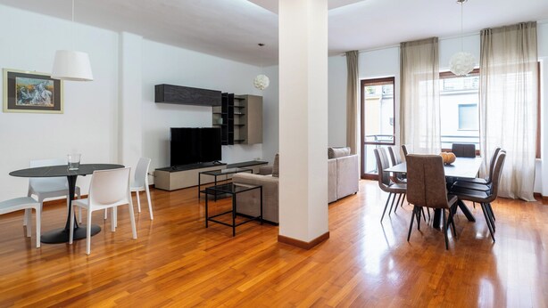 Una sala de estar moderna con comedor, piso de madera, televisor de pantalla plana y sofá.