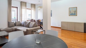 Una sala moderna con un sofá modular, una mesa de centro de vidrio y un comedor con una mesa redonda.