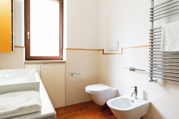 A bathroom with a toilet, bidet, sink, and towel rack.