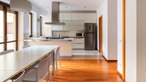 Una cocina moderna con una isla central, electrodomésticos de acero inoxidable y un comedor con mesa y sillas blancas.