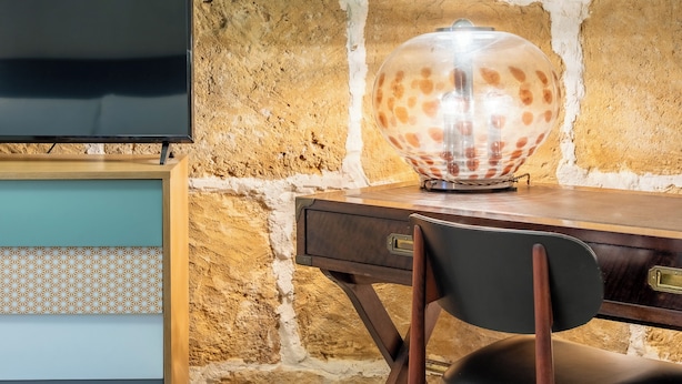 A wooden desk with a transparent globe lamp, a television mounted on a stone wall, and a patterned cabinet below. - Nicu Amuri con Terrazza a Noto by Wonderful Italy (Noto)