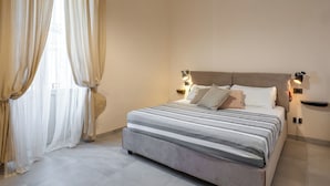 A neatly made bed with a striped bedspread and two pillows, a bedside table with a lamp, and sheer curtains on a window. - Nicu Amuri con Terrazza a Noto by Wonderful Italy (Noto)