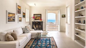 A spacious living room with a white sofa, a glass coffee table, and a view of the sea through an open door. - Villa Plemmiria by the Sea by Wonderful Italy (Syracuse)