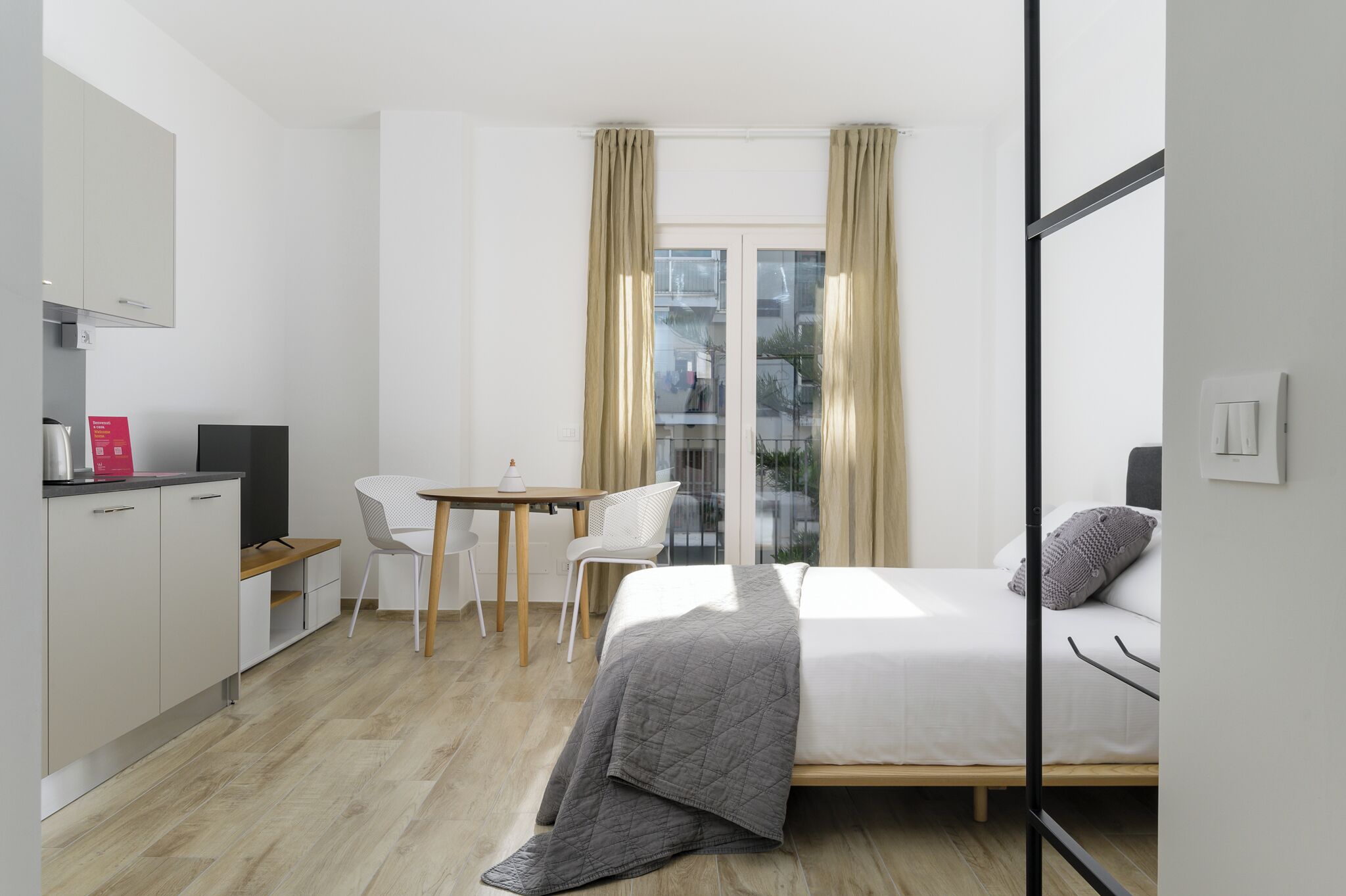 Una camera d'albergo moderna con un letto, una scrivania, una sedia e vista sulla città attraverso ampie finestre.