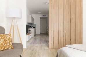 Ein moderner, gut beleuchteter Raum mit Sofa, Stehlampe, Bett und einer Küche im Hintergrund.