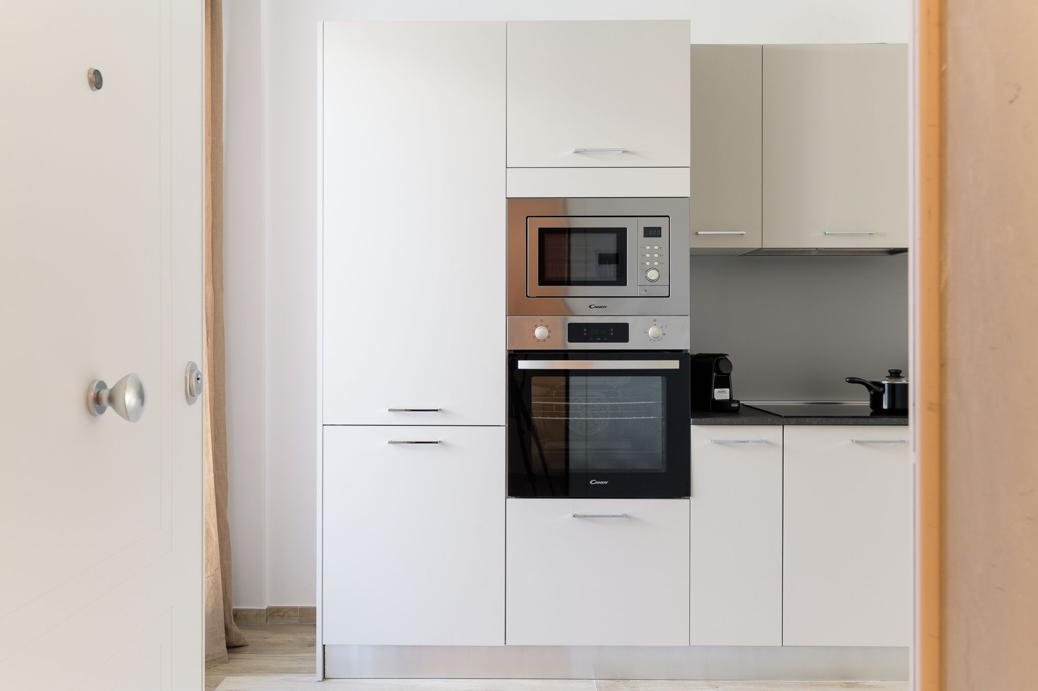 A modern kitchen with white cabinets, a built-in microwave, oven, and a coffee maker.