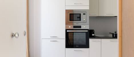 A modern kitchen with white cabinets, a built-in microwave, oven, and a coffee maker.