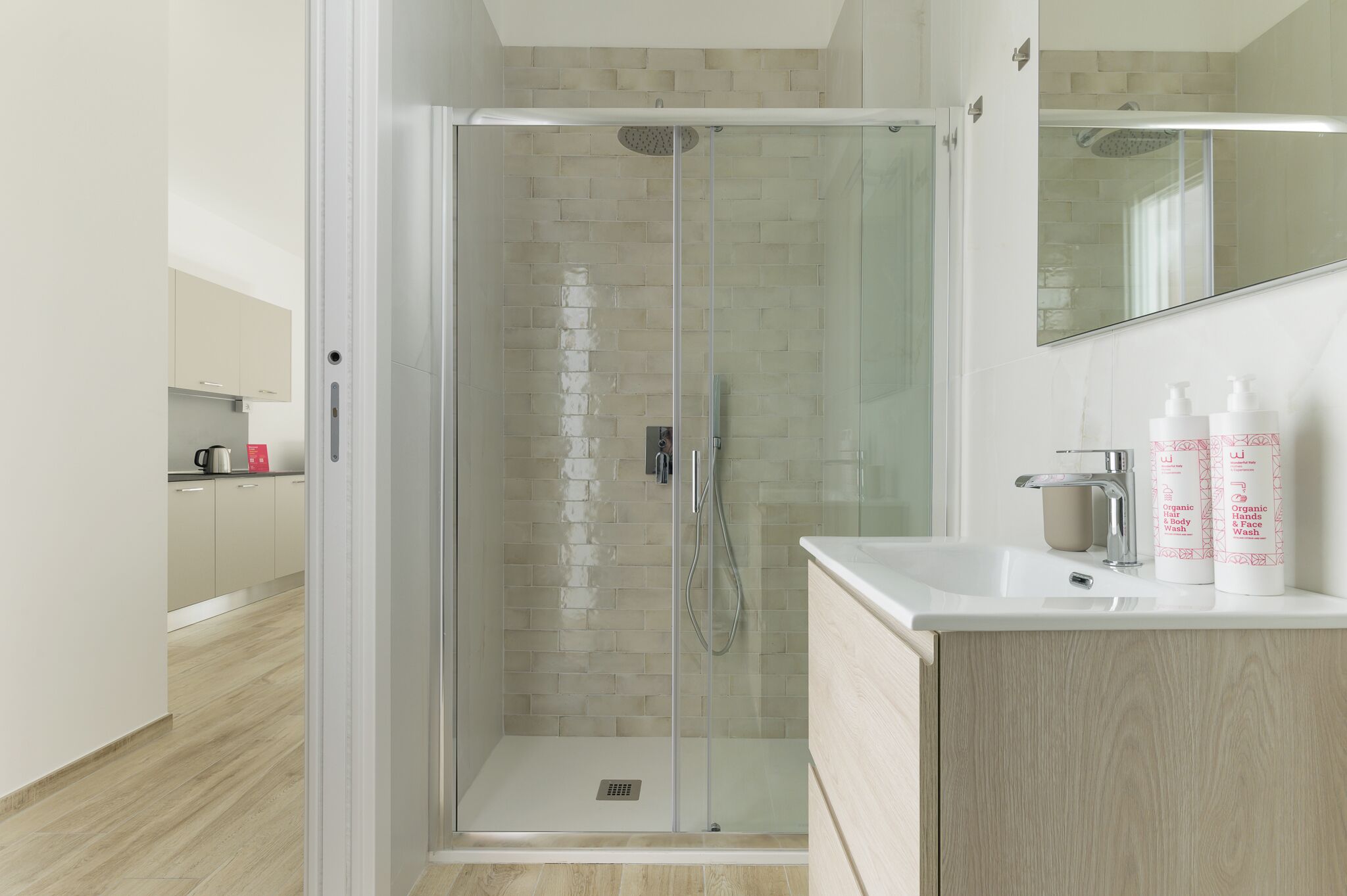 A modern bathroom with a glass-enclosed shower, a sink with toiletries, and a mirror above the sink.
