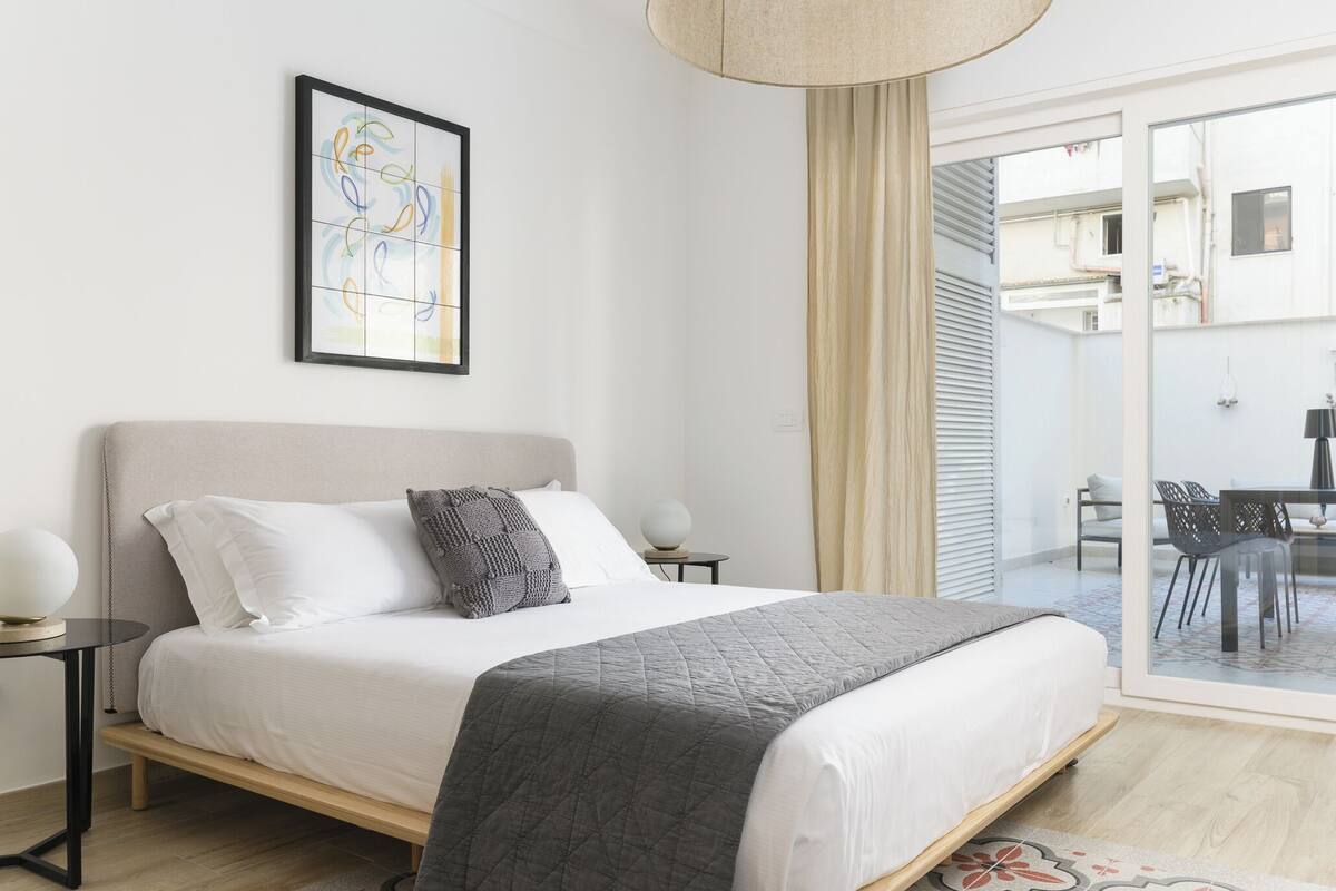 Een moderne slaapkamer met een groot bed, een nachtkastje, een lamp en een lijst met abstracte kunst aan de muur.