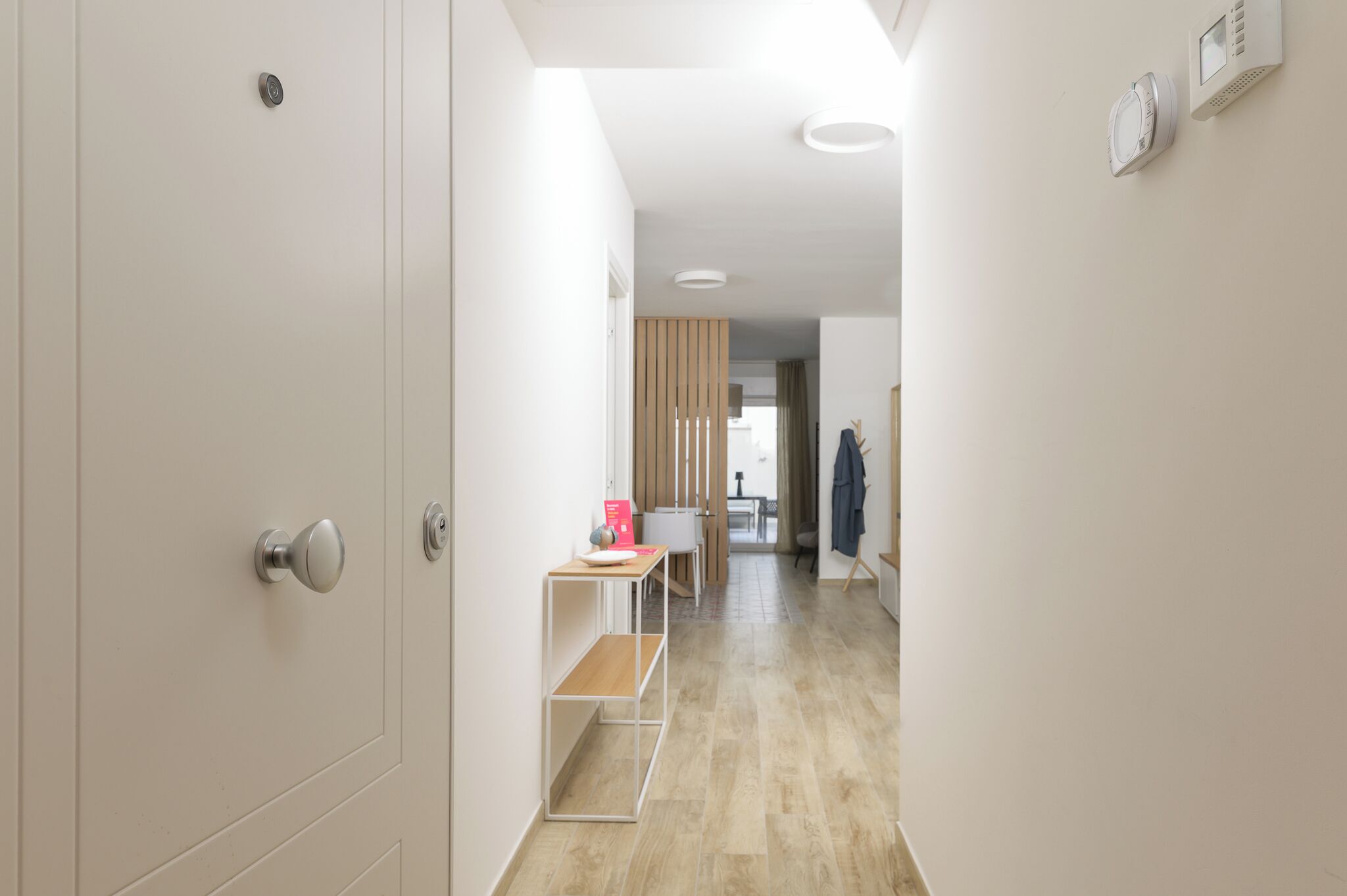 A modern hallway with a wooden floor, a white door, and a small table with a red object on it.