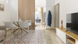 Un salon moderne comprenant un téléviseur, un canapé, un coin repas avec une table et des chaises, ainsi qu’un tapis à motifs.