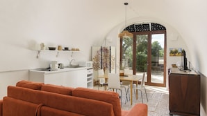 Una sala moderna con un sofá, un comedor con mesa y sillas, una cocina con pileta y electrodomésticos, y un amplio arco que da a un balcón.