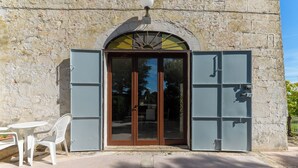 Un edificio de piedra con un amplio arco de entrada, una pequeña mesa con una silla y una lámpara sobre la puerta.