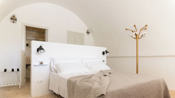 Una cama bien hecha con un edredón color beige, un cabecero blanco y un perchero dorado.