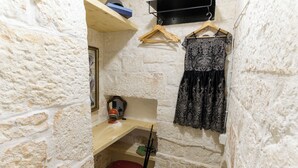 A small, stone-walled room with a wooden desk, a red chair, and a black lace dress hanging on the wall. - Casa del Polpo Blu by Wonderful Italy (Ostuni)