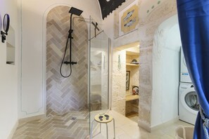 Un baño moderno con ducha de vidrio, un taburete, lavadora y barra para toallas.
