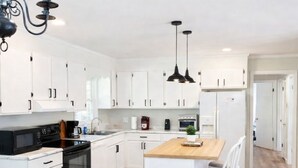 Une cuisine moderne avec des armoires blanches, un îlot central en bois, des appareils électroménagers noirs et des luminaires suspendus.