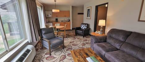 A hotel room with a sofa, a chair, a dining table, and a kitchen area.