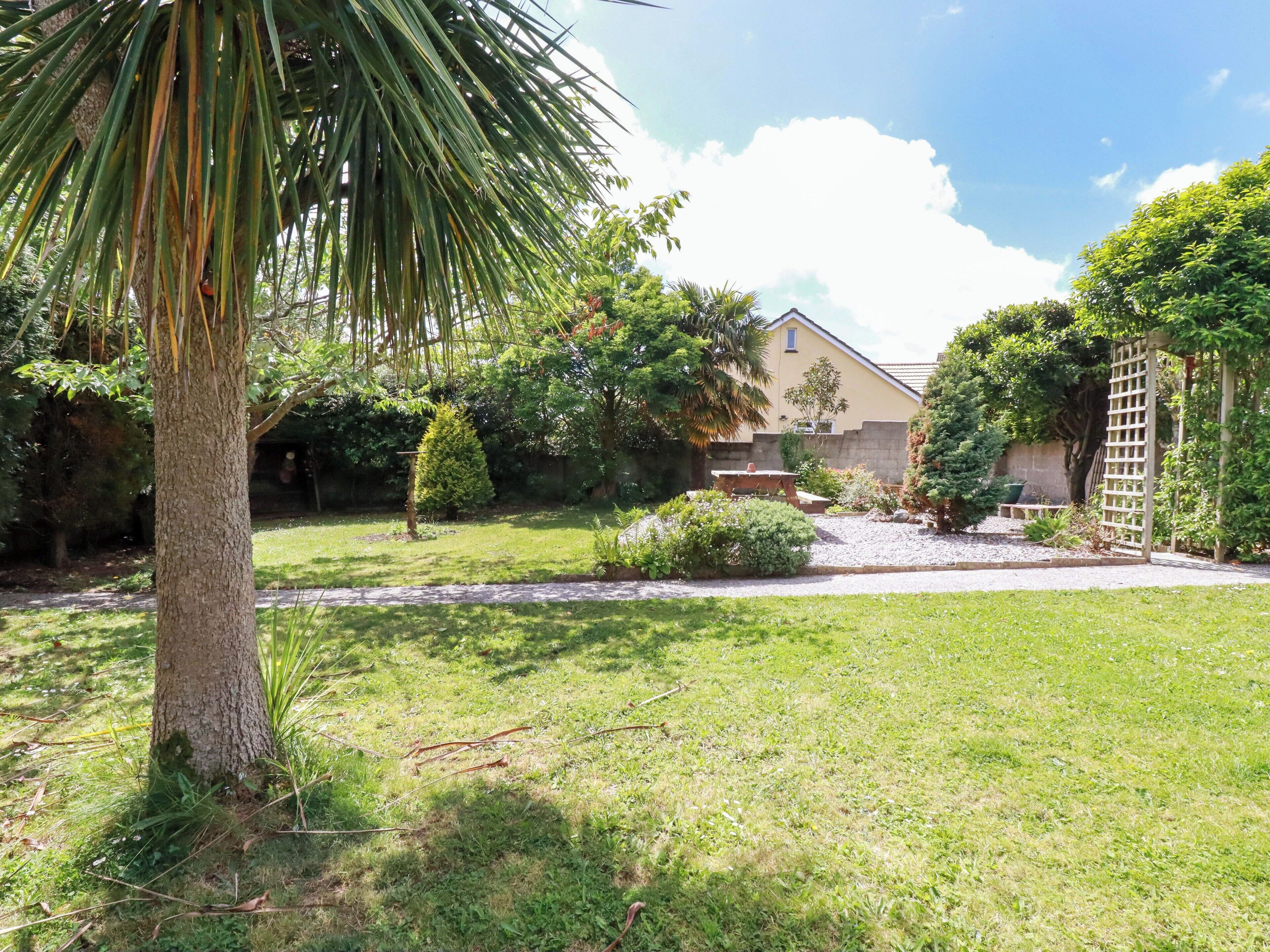 Un jardín cuidado con una palmera, un pequeño estanque y una casa al fondo.