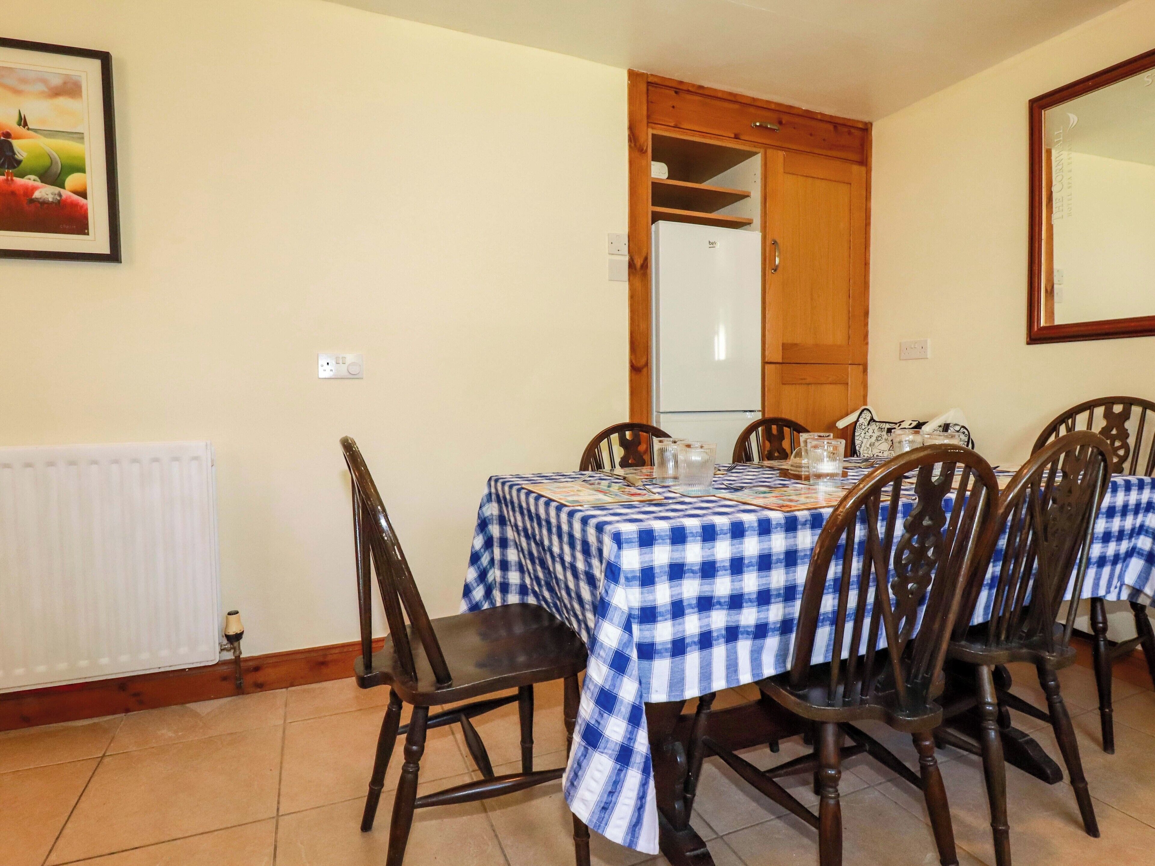 Un'area pranzo con tovaglia a scacchi, sedie di legno e un frigorifero bianco.